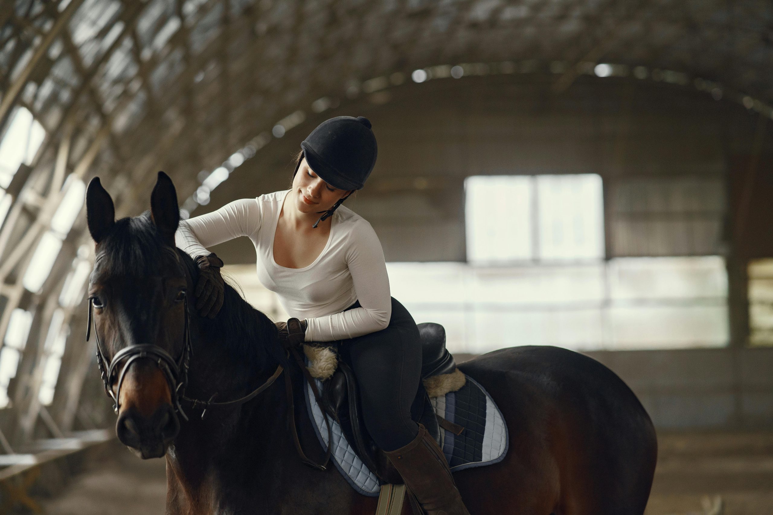 A woman riding a horse in an indoor equestrian arena, wearing a helmet.