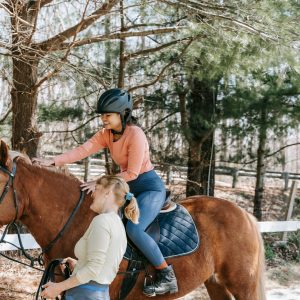 A woman taking horseback riding lessons in a scenic forest with a guide. Outdoor relaxation and training.